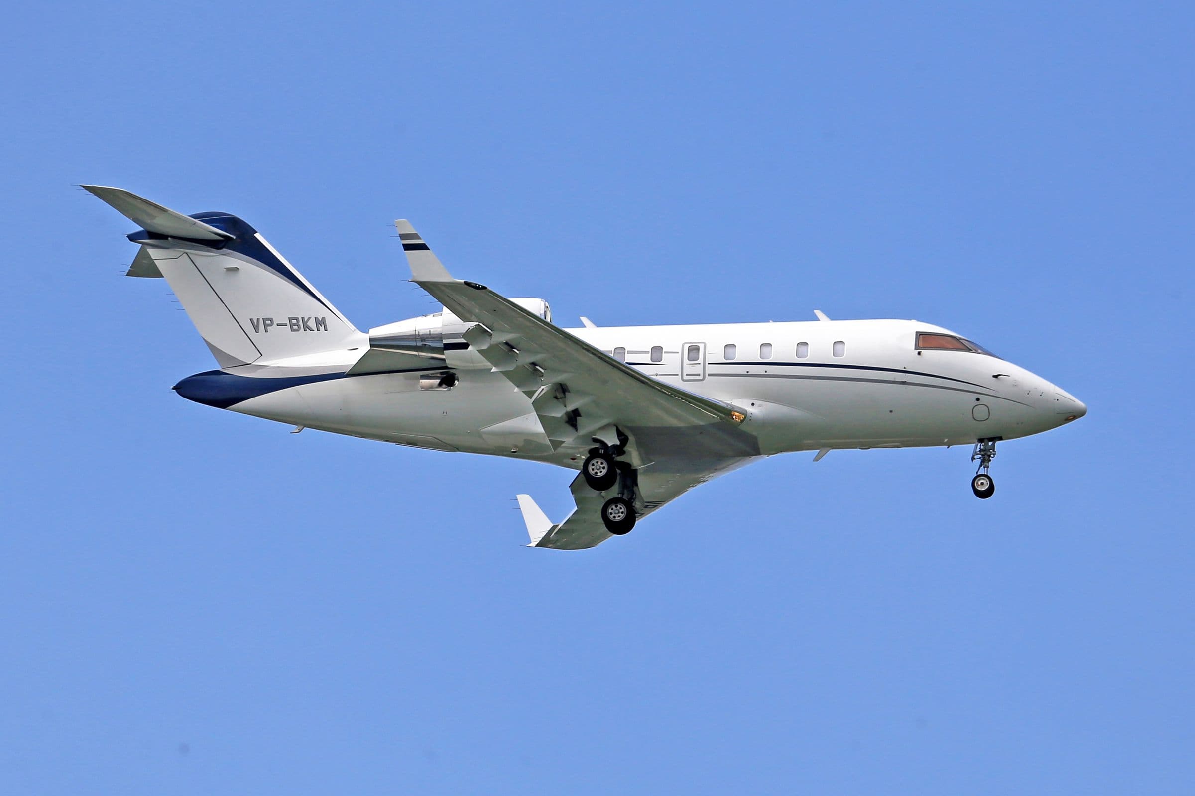 A white business jet in flight against a clear blue sky